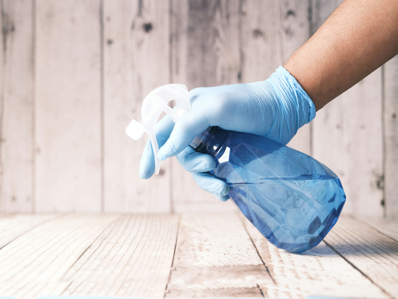 A cleaning professional with gloves on sprays cleaner on a wood surface.