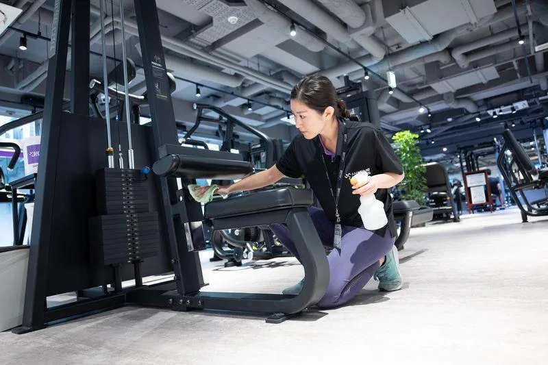Professional commercial cleaner disinfecting fitness equipment inside a modern gym in Charlotte, NC to maintain a clean, healthy workout environment.